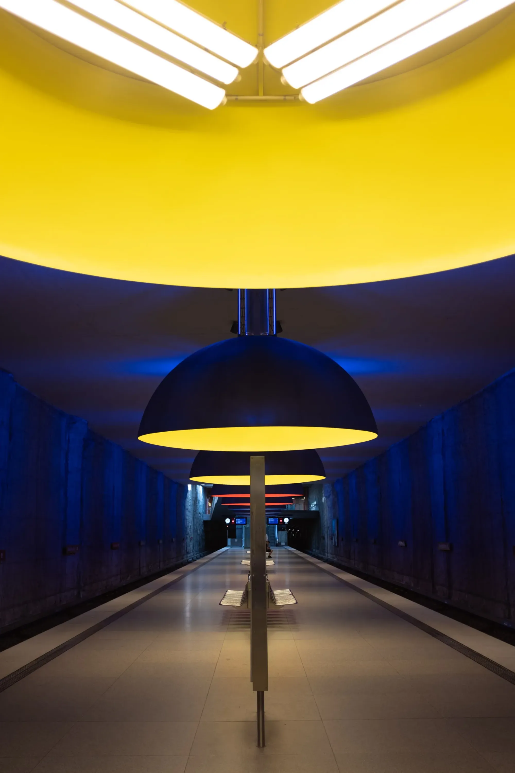 Symmetrischer Blick durch die U-Bahn-Station Westfriedhof München mit blau-gelben Kuppelleuchten