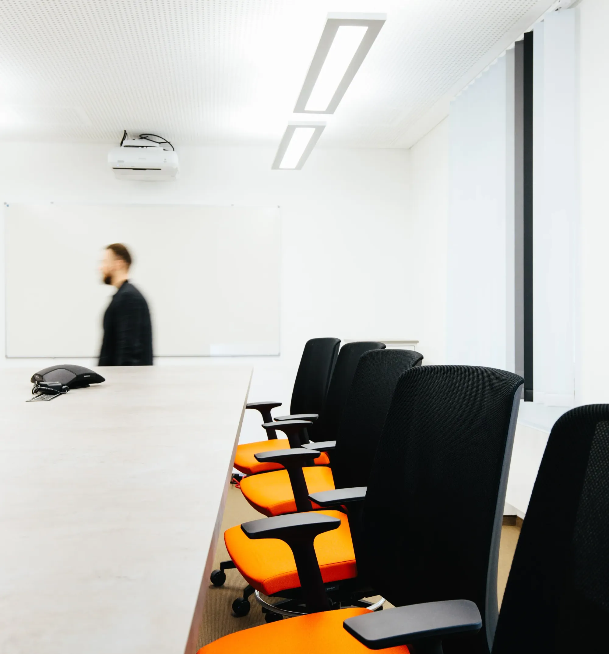 Konferenzraum mit Stuhlreihe, eine Person geht in Bewegungsunschärfe am Whiteboard vorbei