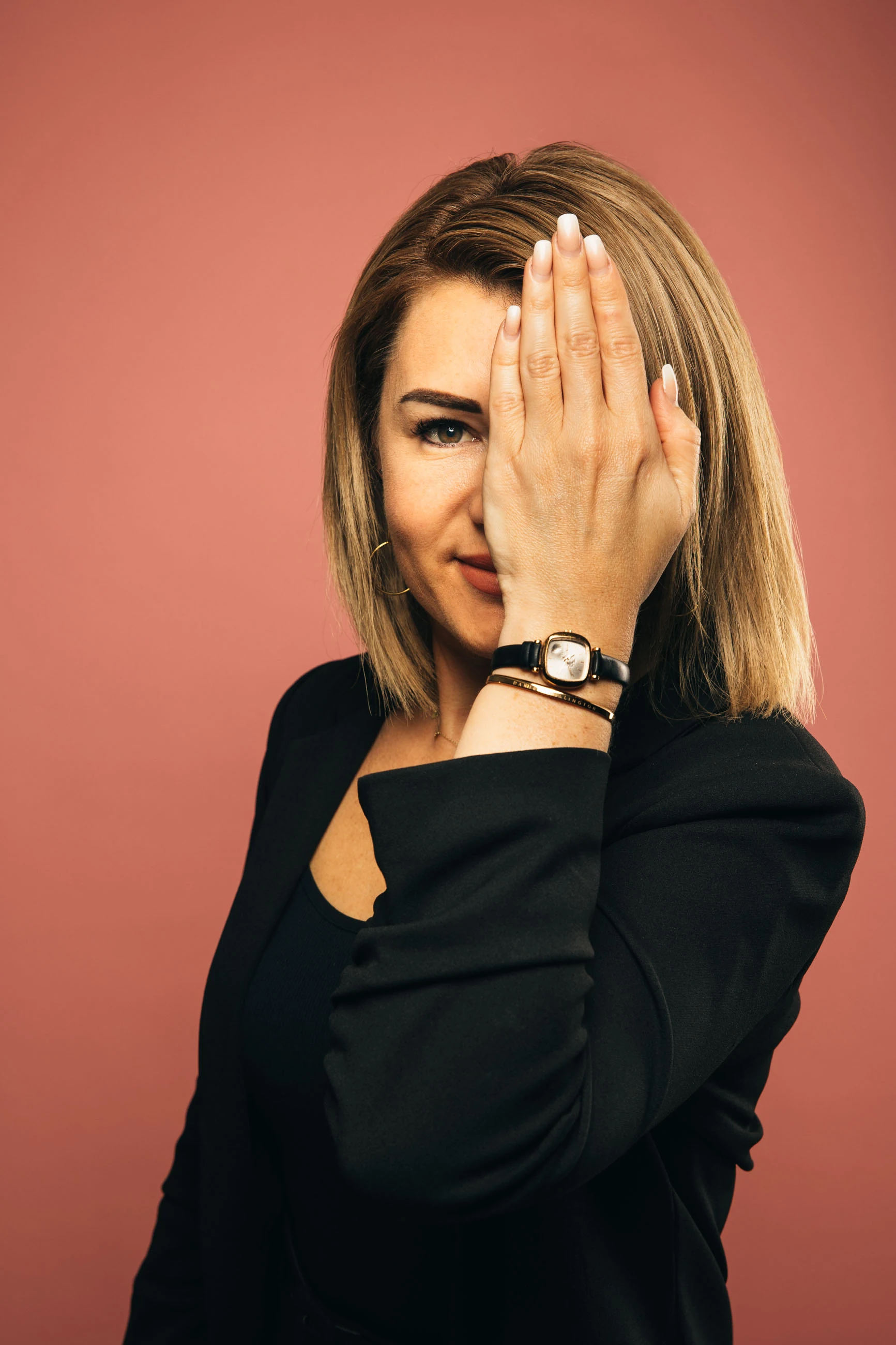Beauty-Porträt einer blonden Frau im schwarzen Blazer vor altrosa Hintergrund