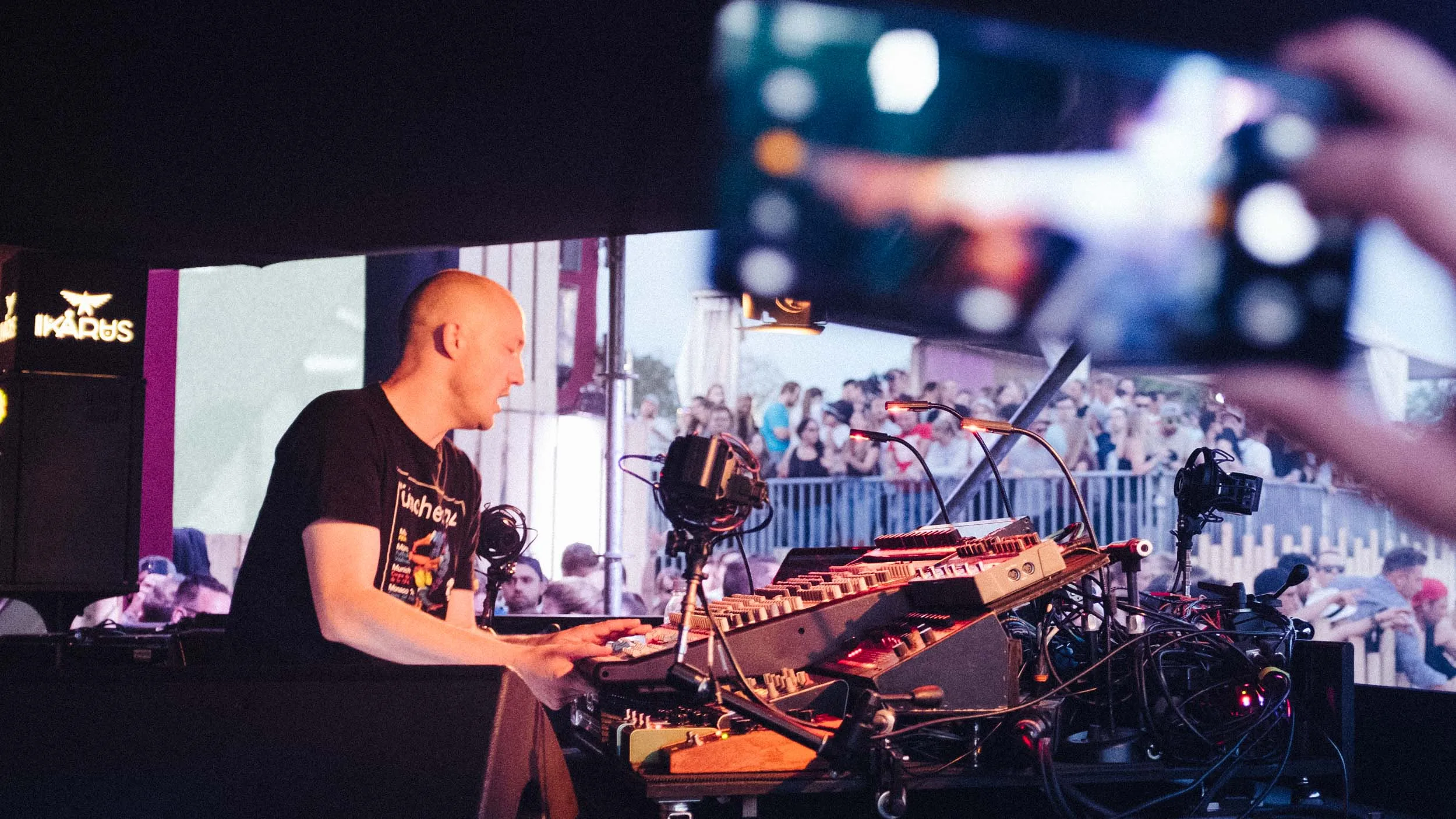 Live-Act am Synthesizer-Setup auf der Festivalbühne, Publikum filmt mit dem Smartphone