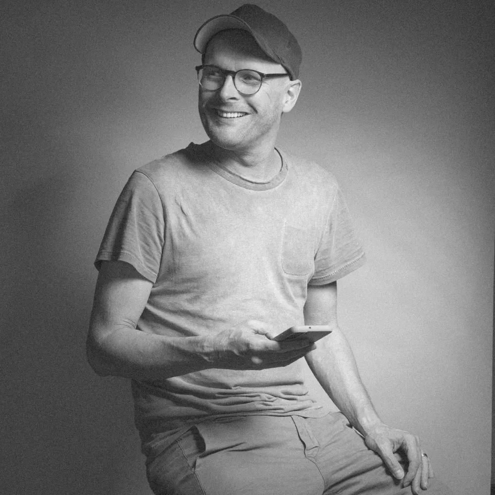 Jörg Tenhündfeld, Gründer von tenfield. mediendesign in Memmingen, lachend mit Smartphone in der Hand – Schwarzweiß-Porträt