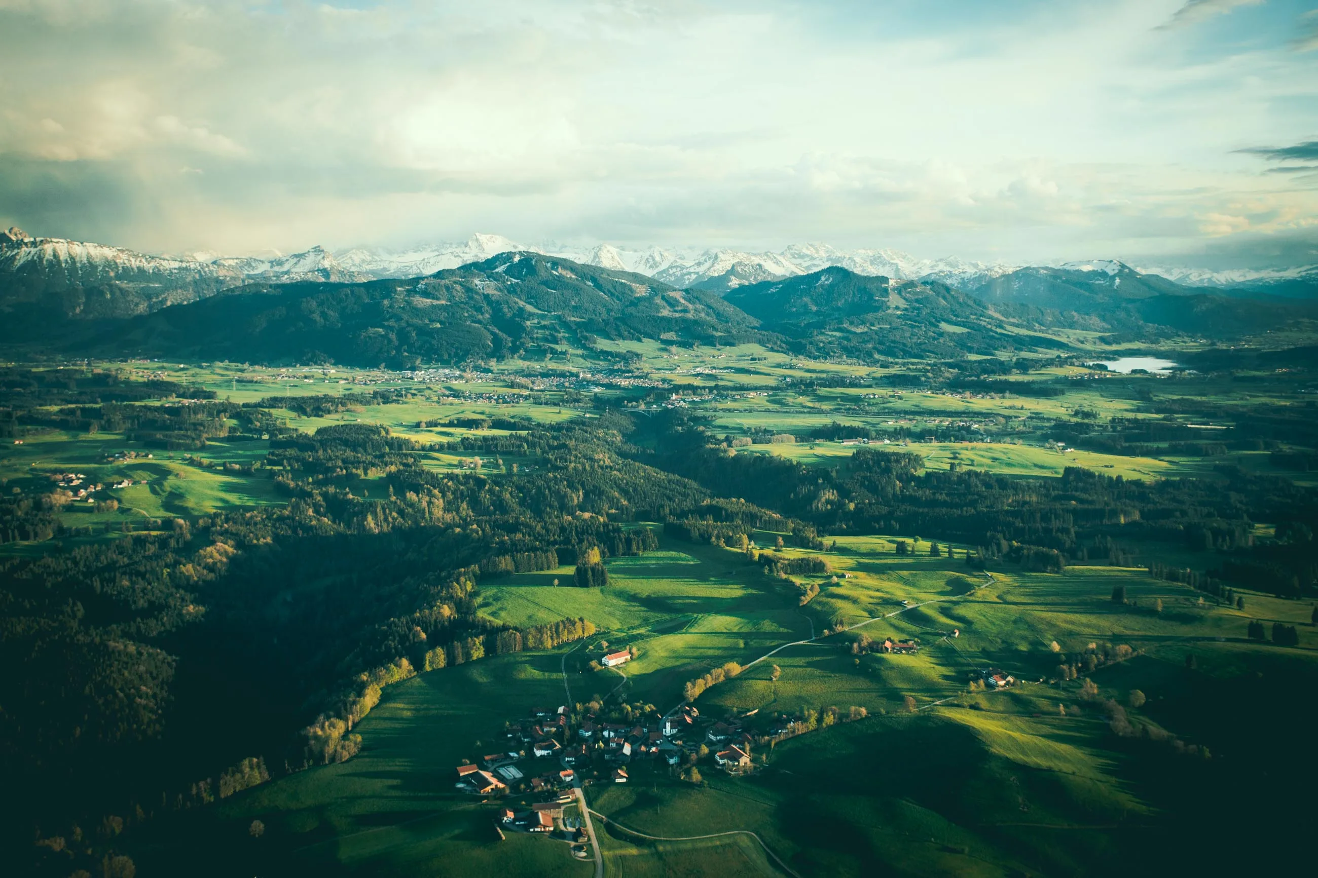 Luftaufnahme der grünen Allgäu-Landschaft mit Dörfern und schneebedeckten Alpen