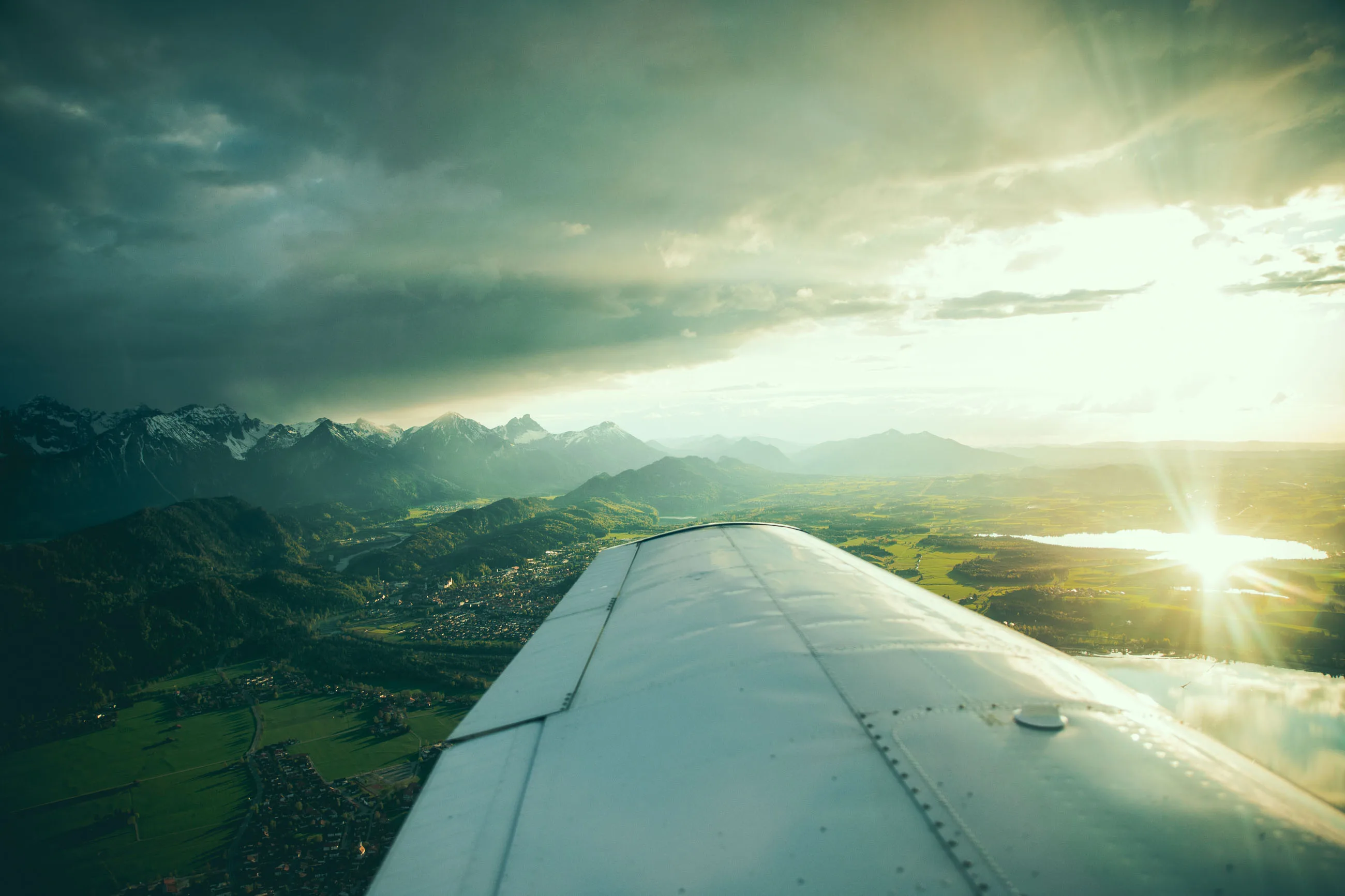 Blick aus dem Kleinflugzeug über die Tragfläche auf die sonnenbeschienene Allgäu-Landschaft