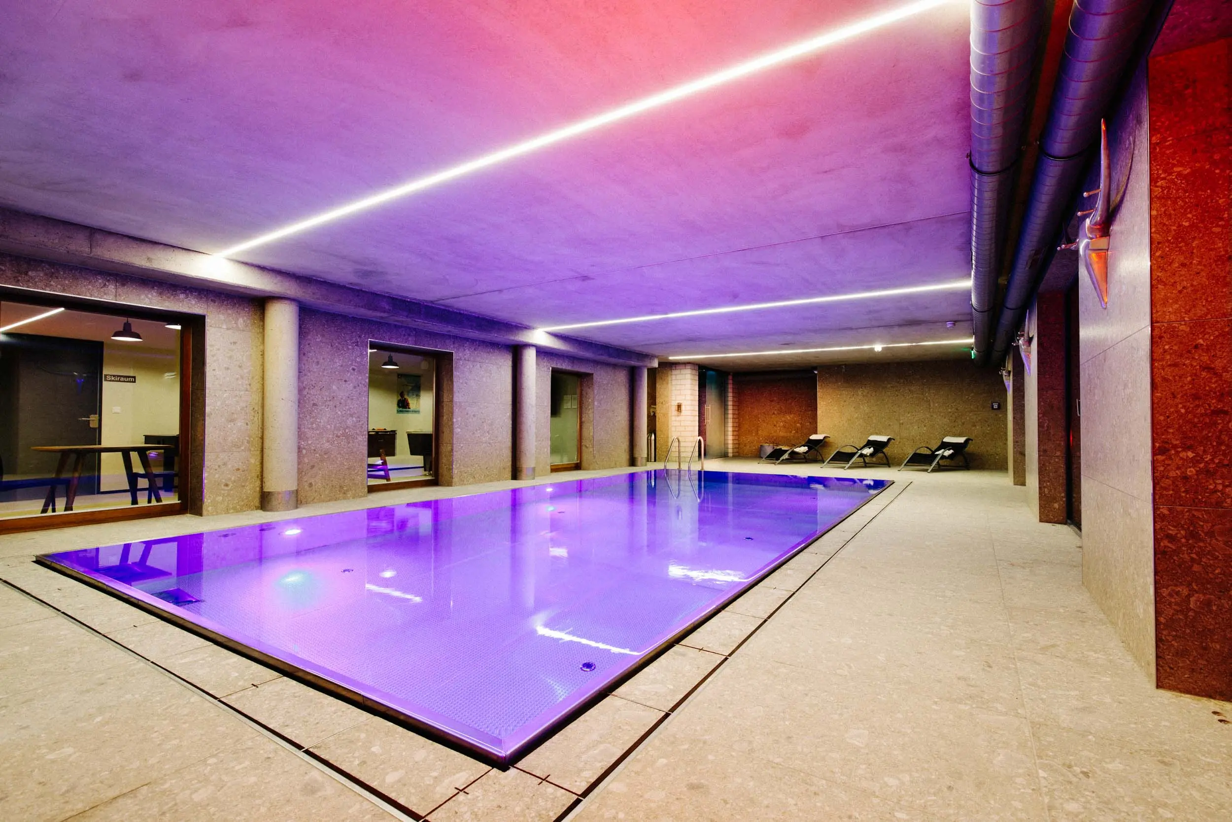 Hallenbad mit farbiger LED-Beleuchtung in Violett und Pink, Liegen am Beckenrand